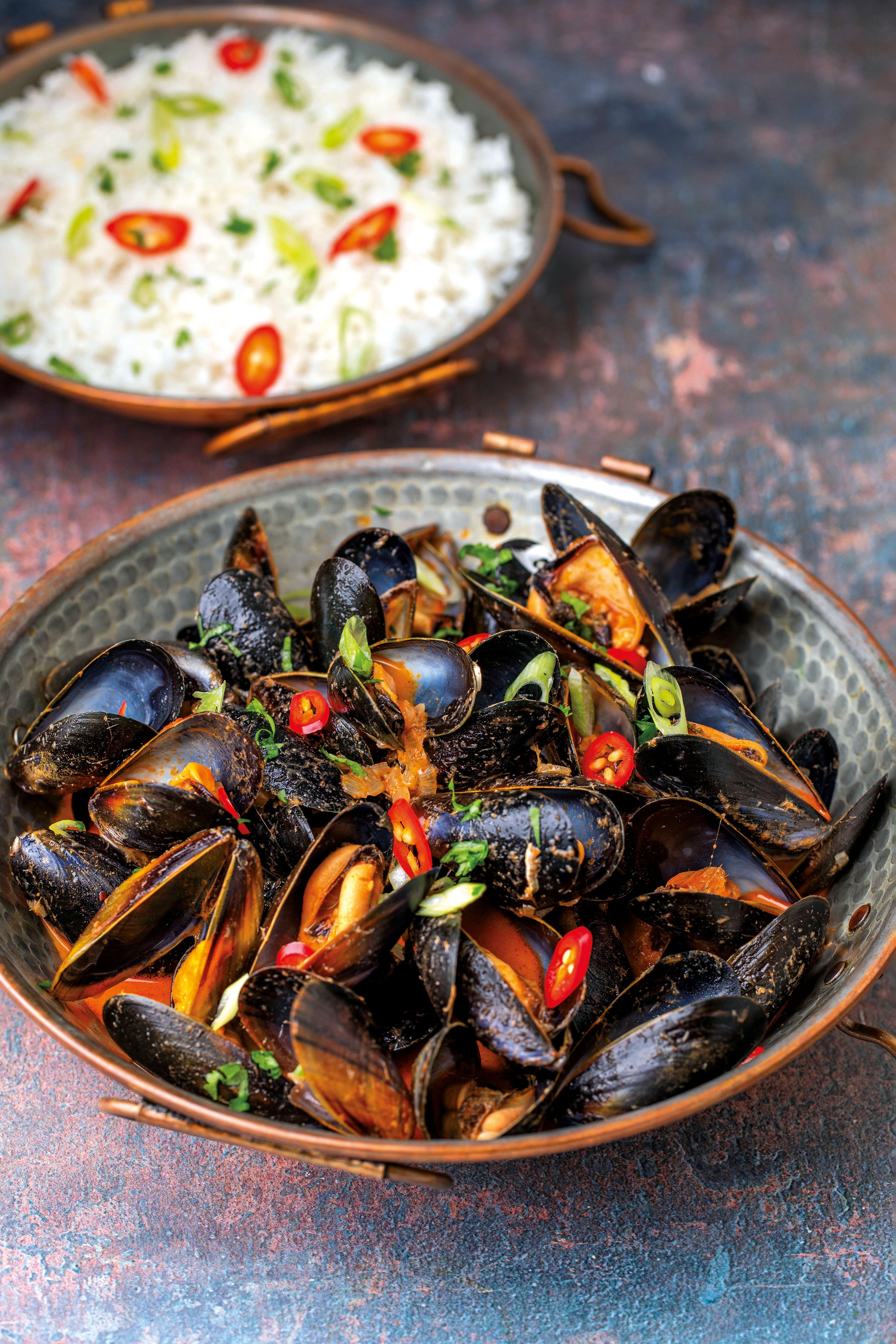 A bowl of Thai red curry mussels with a bowl of rice in the background