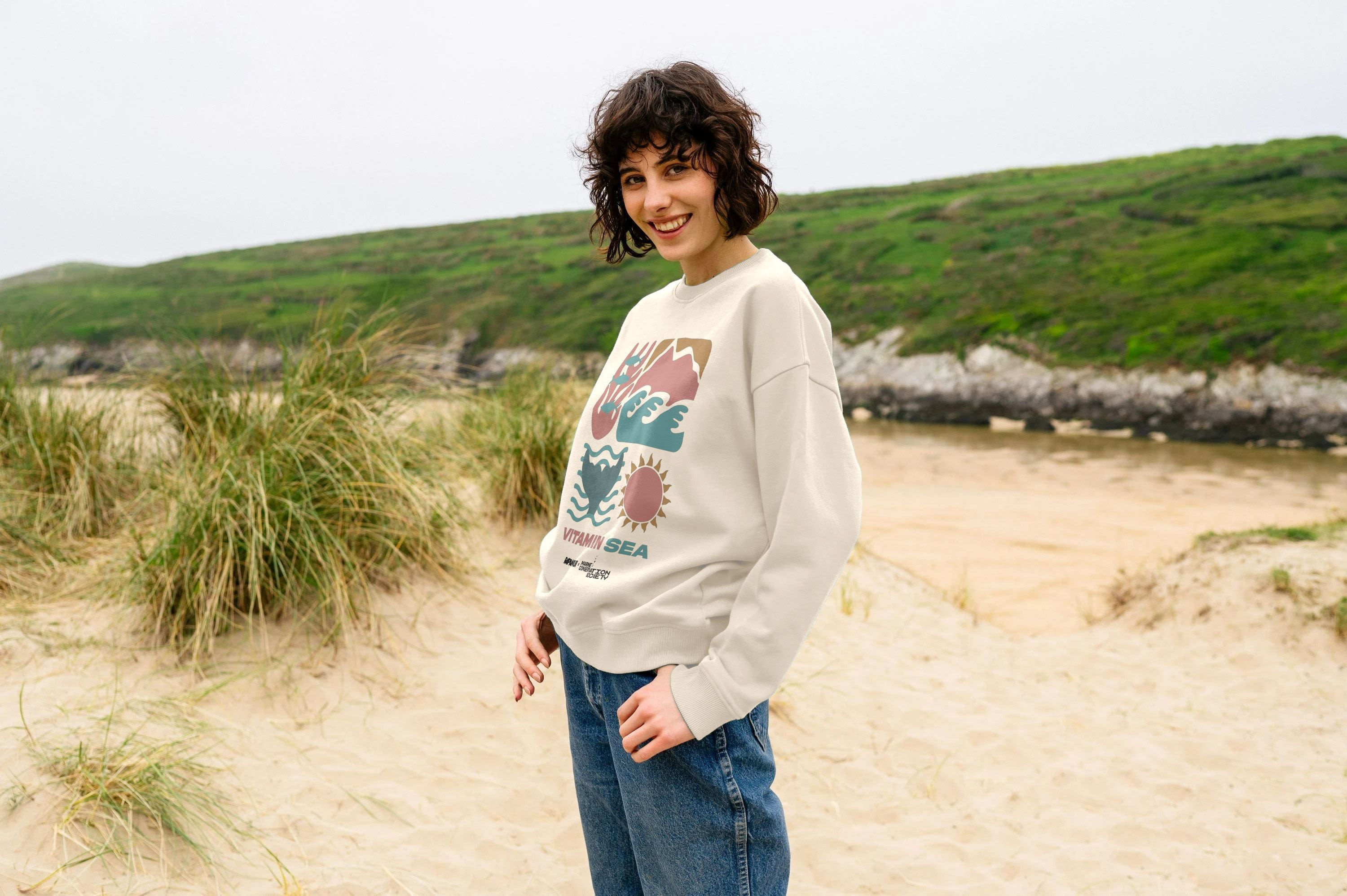 A woman modelling a Vitamin Sea jumper standing on the beach