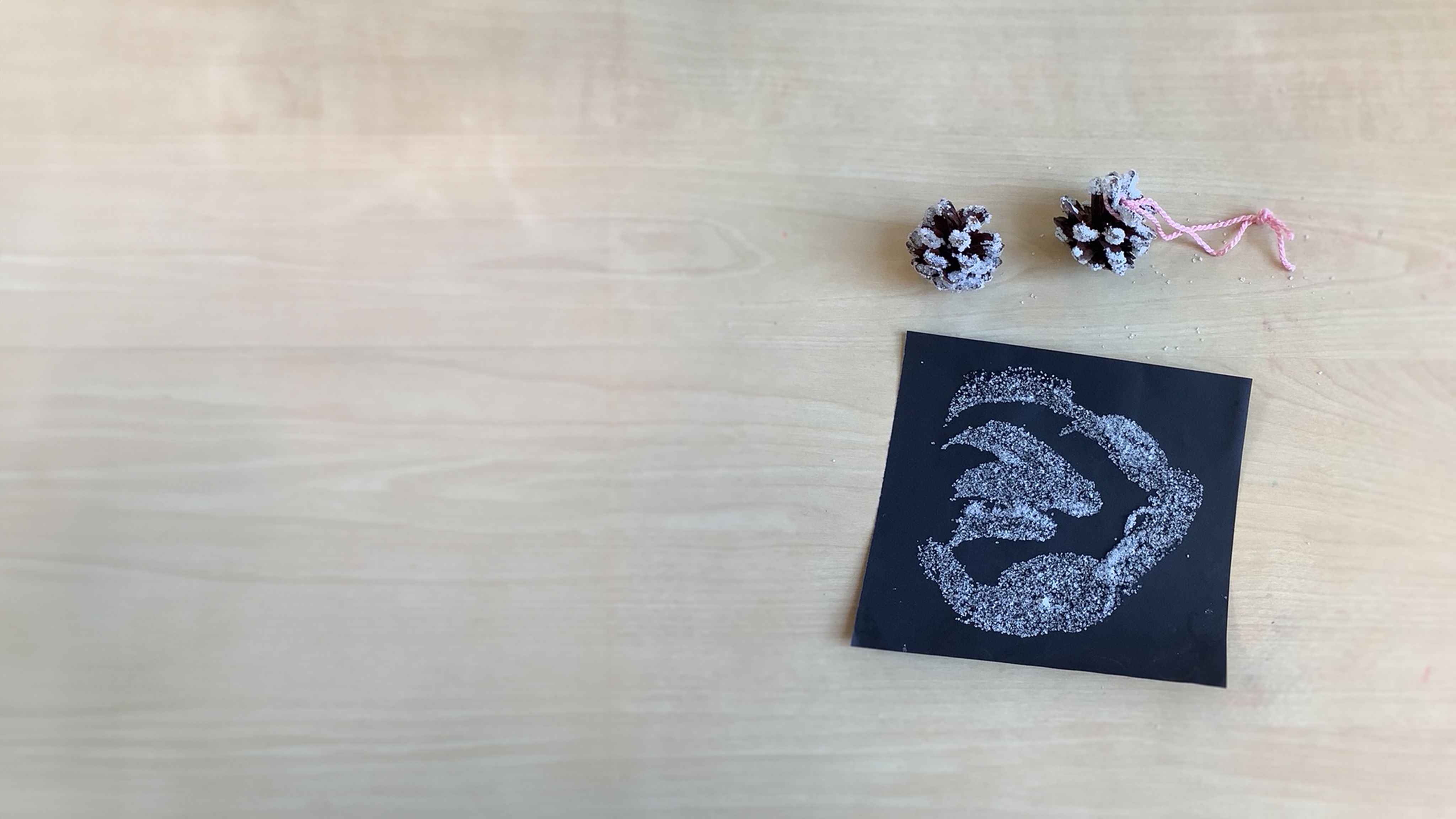 Two pine cone decorations which have been dipped in sugar and a picture showing sugar stuck on black paper as an alternative to glitter.